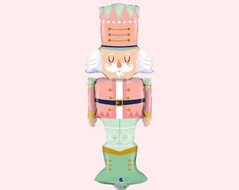 May include: A pink and green nutcracker balloon with a white beard and mustache. The balloon has a gold belt and a green hat with gold trim.