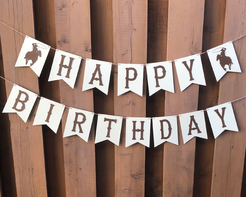 May include: White banner with brown letters spelling "Happy Birthday" with a cowboy silhouette on each end.