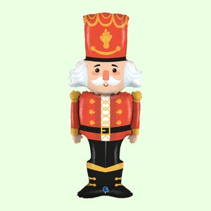 May include: A foil balloon shaped like a nutcracker soldier. The figure wears a tall red hat with gold trim, a red jacket with gold buttons and white cross-hatching, a black belt, and black boots. It has white hair, a moustache, and a peach face.