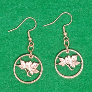 May include: A pair of silver dangle earrings with a round coin-shaped charm featuring a cut-out design of two maple leaves.