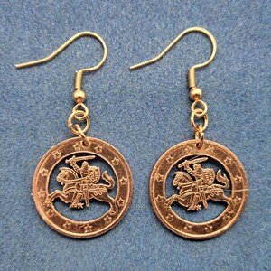May include: A pair of gold-toned earrings featuring a Lithuanian coin with a cutout design of a knight riding a horse. The coin is surrounded by a circle of stars.