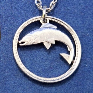 Może przedstawiać: Srebrny naszyjnik z monetą, w której wycięto kształt skaczącej ryby. Moneta jest na srebrnym łańcuszku.