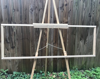 Puede incluir: Un marco de telar de madera en un caballete de madera. El telar está hecho de madera natural y tiene una cuerda blanca atada.