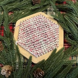 May include: A hexagonal loom with white and pink yarn woven into a checkered pattern. The loom is made of wood and has a natural finish.