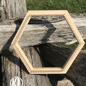 May include: A hexagonal wooden loom with metal pegs around the perimeter. The loom is resting on a stack of weathered wooden logs.