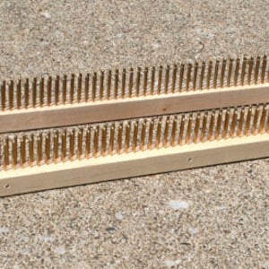 Puede incluir: Dos marcos de madera con filas de dientes de metal dorado. Los marcos se utilizan para tejer hilo.