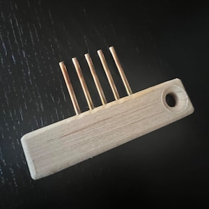 May include: A wooden tool with five metal prongs, used for weaving.