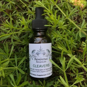 May include: A brown glass bottle with a black dropper top and a white label. The label says "Reverence Botanicals" and "Cleavers". The label also says "Made with: Aerial parts of Galium aparine extracted in 60% organic cane alcohol" and "Herbal Dietary Supplement 1 fl oz - 30 ml".