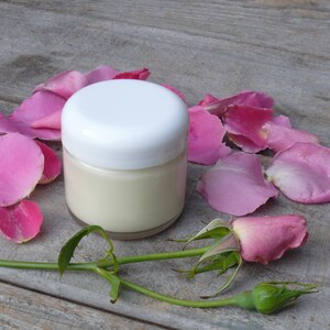 Puede incluir: Un tarro blanco de crema con un fondo de p&eacute;talos de rosa rosa. El tarro tiene una tapa blanca y est&aacute; lleno de crema blanca.