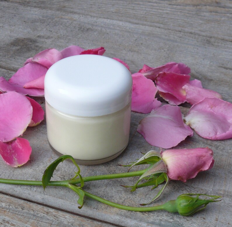 Puede incluir: Un tarro blanco de crema con un fondo de p&eacute;talos de rosa rosa. El tarro tiene una tapa blanca y est&aacute; lleno de crema blanca.