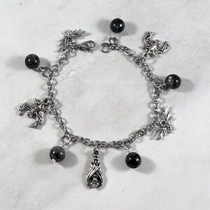 May include: A silver charm bracelet with black beads and bat, dragon, and crescent moon charms.