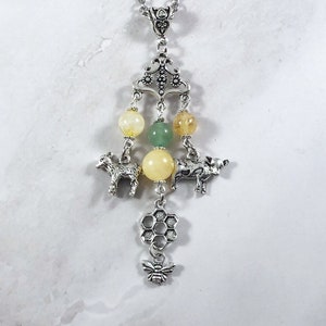 Op de afbeelding: Een zilveren ketting met een bedel met een honingraat, een bij en twee kleine dierfiguren. De bedel is bevestigd aan een zilveren hanger met drie gele en groene kralen.