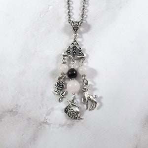 Puede incluir: Un collar de cadena de plata con un colgante de plata que presenta una rosa, un ciervo y una granada. El colgante est&aacute; adornado con cuentas rosas y negras.