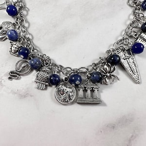 May include: A silver charm bracelet featuring blue beads and a variety of charms, including a snake, an owl, a spider, a temple, and a crescent moon.