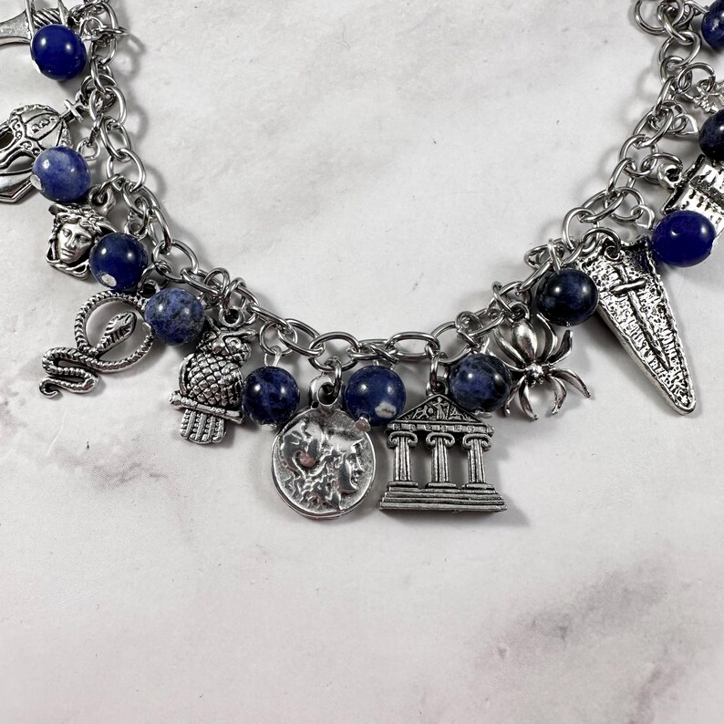May include: A silver charm bracelet featuring blue beads and a variety of charms, including a snake, an owl, a spider, a temple, and a crescent moon.