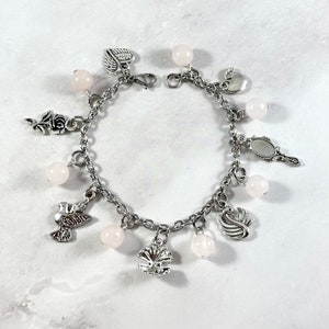 May include: A silver charm bracelet with pink beads and various charms, including a bird, a swan, a heart, a rose, an apple, and a mirror.