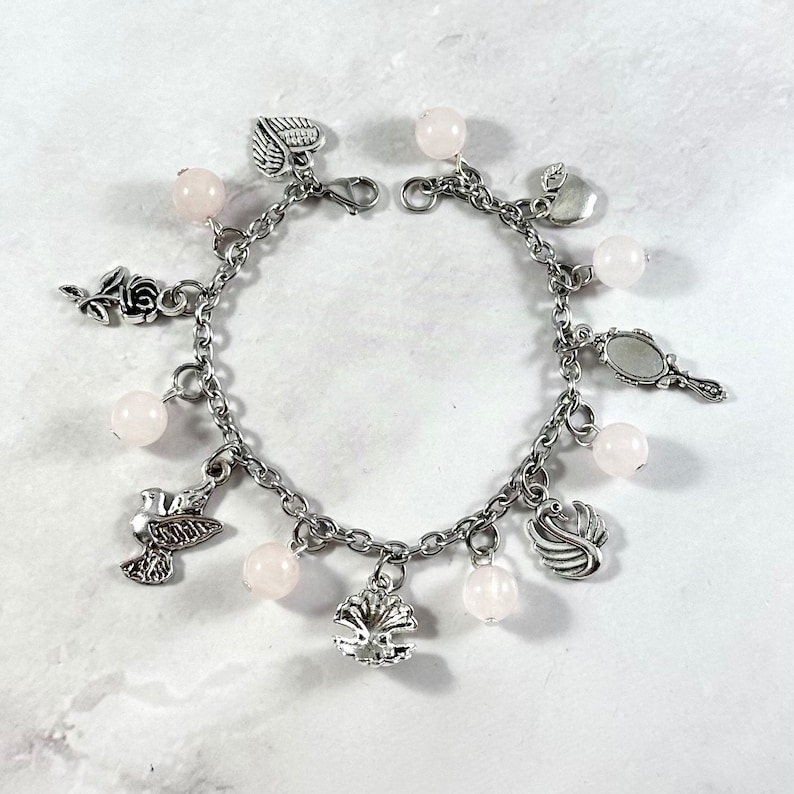 May include: A silver charm bracelet with pink beads and various charms, including a bird, a swan, a heart, a rose, an apple, and a mirror.