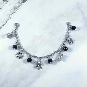 May include: A silver charm bracelet with black beads and Halloween-themed charms, including spiders, spiderwebs, and spools of thread.