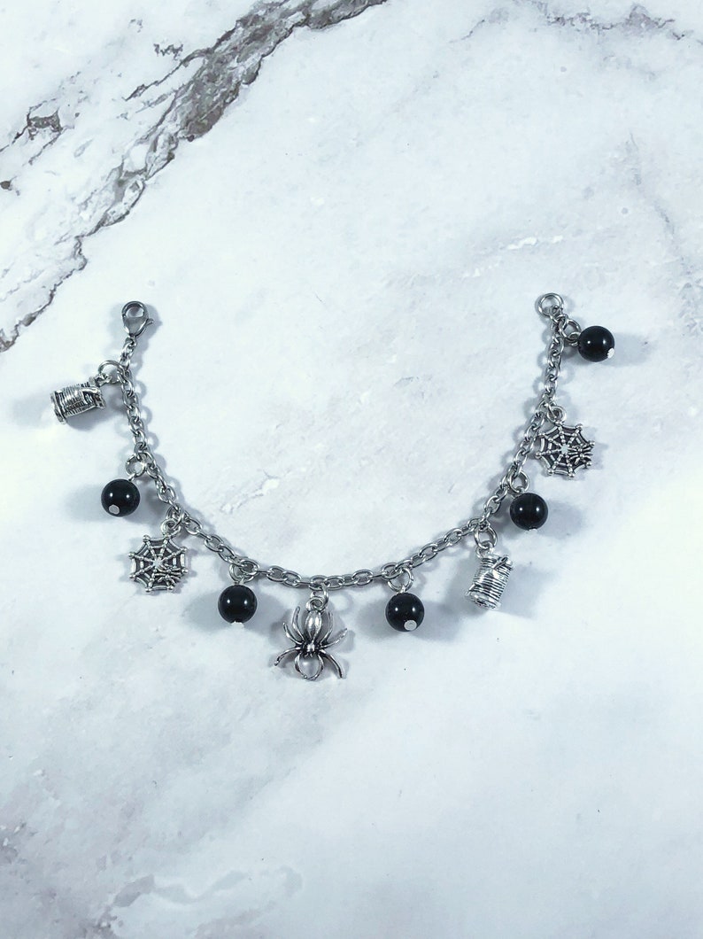 May include: A silver charm bracelet with black beads and Halloween-themed charms, including spiders, spiderwebs, and spools of thread.