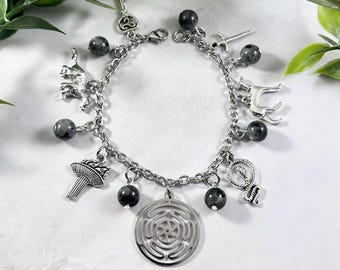 May include: A silver charm bracelet with black beads and various charms, including a key, a torch, a snake, a wolf, a labyrinth, and a sword.