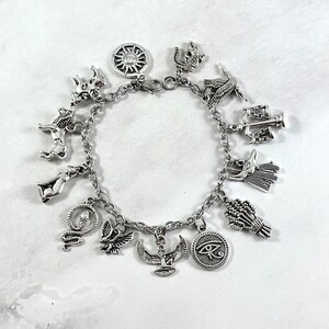May include: Silver charm bracelet with various Egyptian-themed charms, including a sun, an ankh, a scarab beetle, a cobra, a cat, a lion, a falcon, a scale, a wheat sheaf, and an eye of Horus.