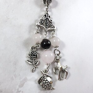 Puede incluir: Un collar con dije de plata con dijes de rosa, ciervo y granada. El collar tambi&eacute;n tiene cuentas rosadas y negras.