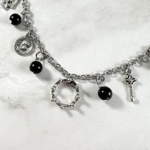 May include: A silver chain bracelet with multiple charms, including a small crown, a key, and black beads.