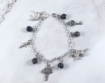 May include: A silver charm bracelet with dark grey beads and various silver charms, including a deer, a key, a sword, a mushroom, and a wolf.