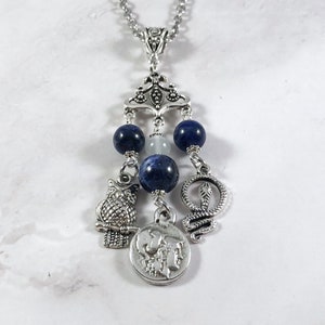 May include: Silver necklace with a blue and white stone charm, an owl charm, a snake charm, and a coin charm with a profile of a woman on it.