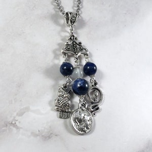 May include: Silver necklace with a blue and white stone pendant. The pendant features an owl, a snake, and a coin charm.