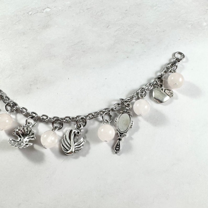 May include: A silver charm bracelet with pink beads and charms, including a swan, a mirror, and a heart.