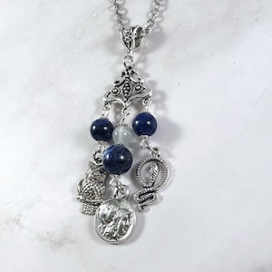 May include: A silver necklace with a pendant featuring a silver owl, snake, and coin charm. The pendant is adorned with blue and white beads.