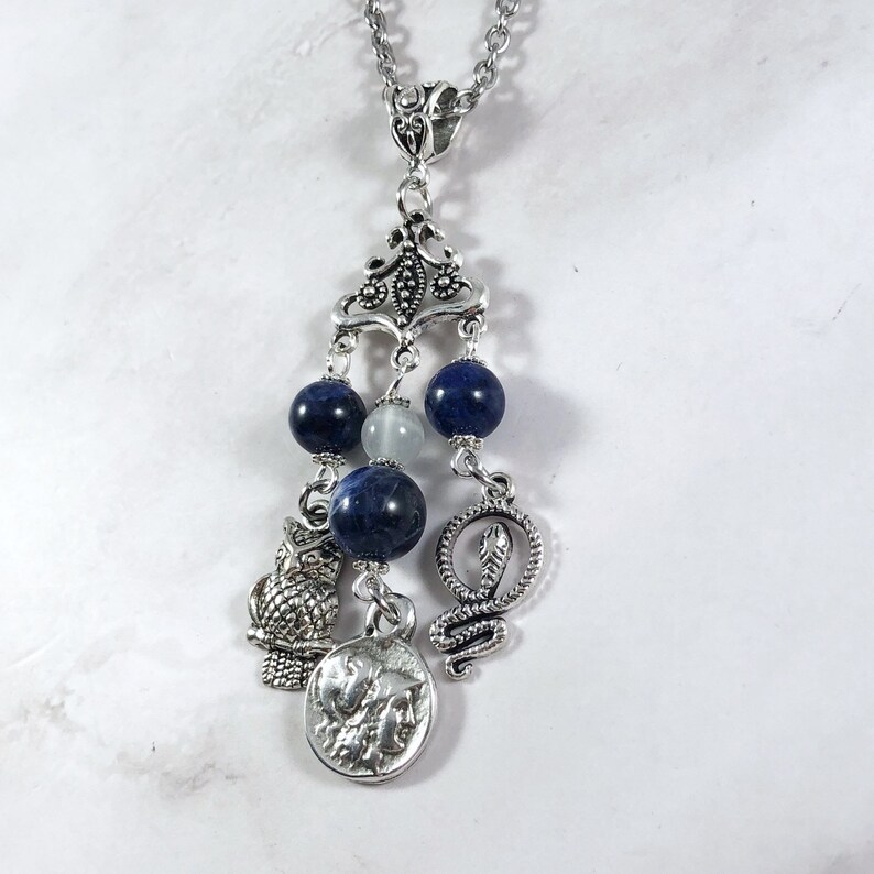 May include: A silver necklace with a pendant featuring a silver owl, snake, and coin charm. The pendant is adorned with blue and white beads.