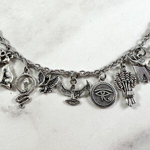May include: Silver charm bracelet with Egyptian themed charms, including a cat, snake, bird, ankh, eye of Horus, and wheat.