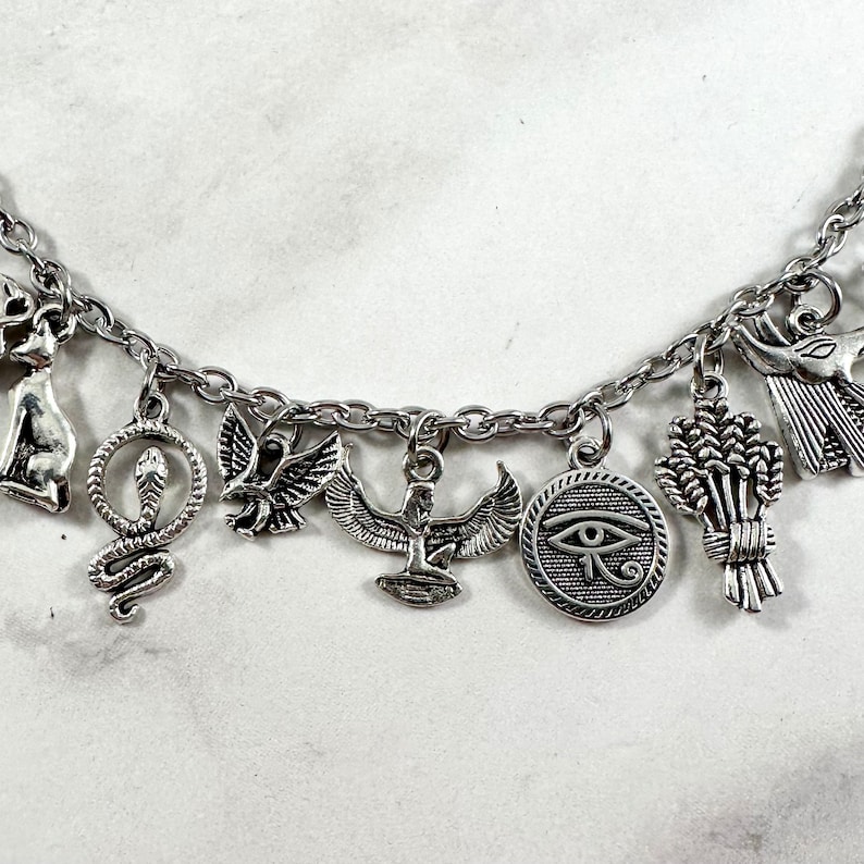 May include: Silver charm bracelet with Egyptian themed charms, including a cat, snake, bird, ankh, eye of Horus, and wheat.
