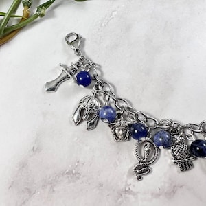 May include: A silver charm bracelet featuring blue gemstone beads and a variety of silver charms, including a sword, a helmet, a face, a snake, and an owl.