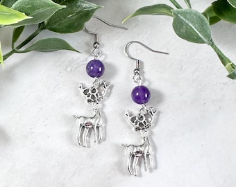 May include: A pair of silver dangle earrings with amethyst beads and a deer charm. The deer charm is a detailed design with antlers and a body.
