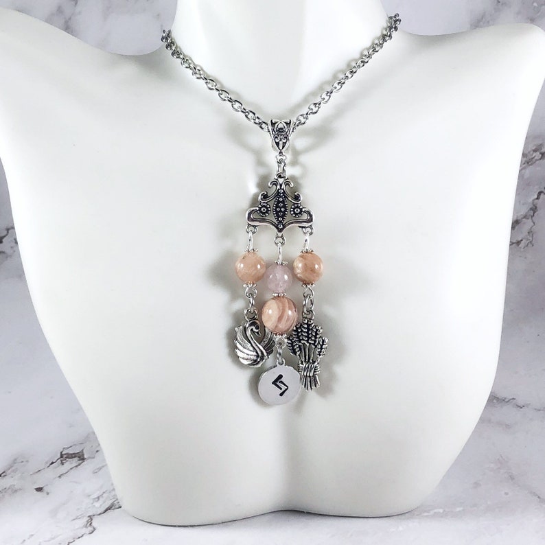 May include: A silver chain necklace with a pendant featuring a silver crown, pink and white beads, a silver swan charm, a silver wheat charm, and a silver charm with the rune "Algiz" engraved on it.