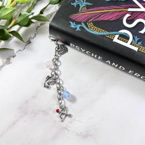 May include: A silver bookmark chain with charms, including a wing, a heart with an arrow, a small figure, and three beads in pink, blue, and light blue.