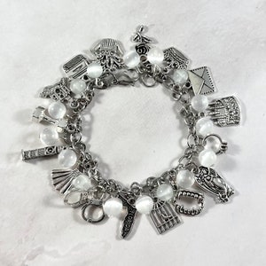 May include: A silver charm bracelet with various charms, including a cage, fangs, and a Florida charm. The bracelet also features white, round beads and is displayed on a white surface.