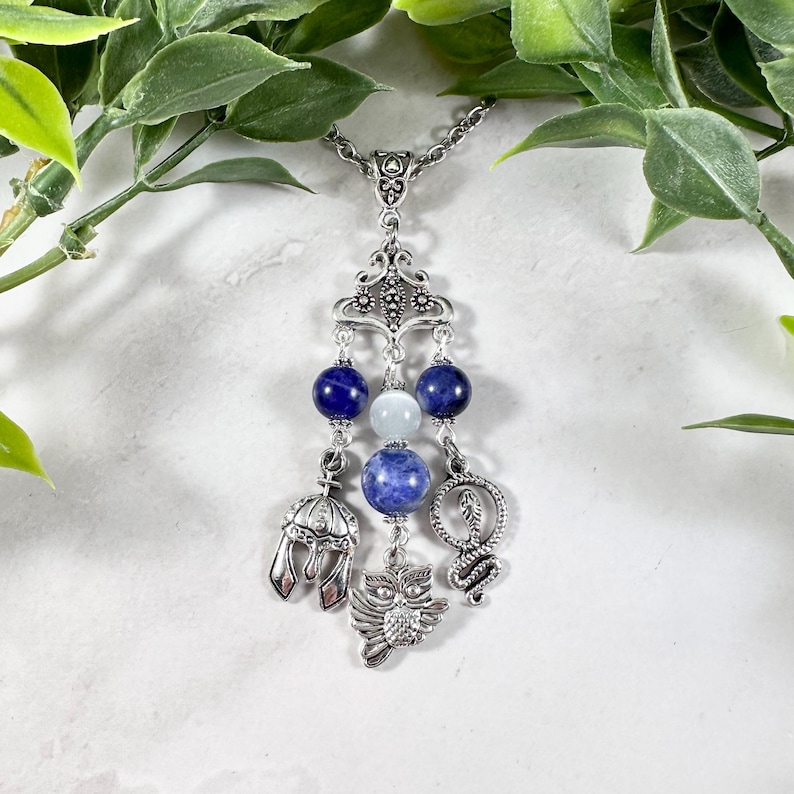 May include: A silver necklace with a pendant featuring blue and white beads, a silver owl charm, a silver snake charm, and a silver helmet charm.