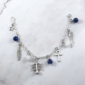 May include: A silver charm bracelet with multiple charms, including a feather, a star, a scale of justice, a cross, a wing, and blue beads.