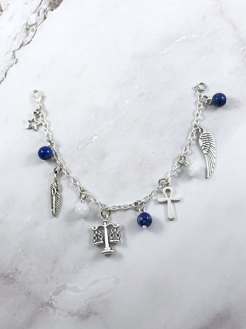 May include: A silver charm bracelet with multiple charms, including a feather, a star, a scale of justice, a cross, a wing, and blue beads.