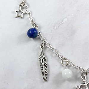 May include: A silver charm bracelet with a blue lapis lazuli bead, a white bead, a feather charm, a star charm, and an anchor charm.