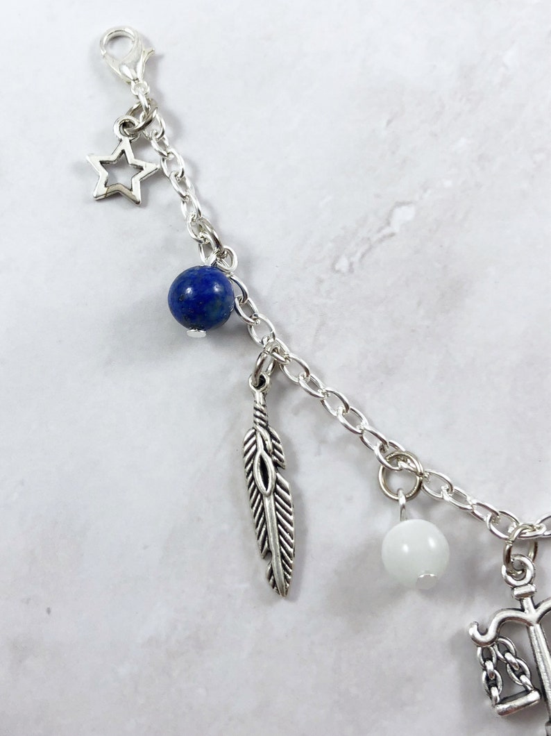 May include: A silver charm bracelet with a blue lapis lazuli bead, a white bead, a feather charm, a star charm, and an anchor charm.