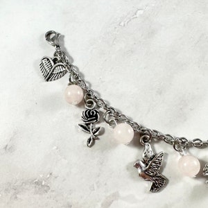 May include: A silver charm bracelet with pink beads, a heart charm, a rose charm, and a dove charm.