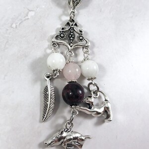 May include: A silver charm necklace with a variety of charms, including a feather, a boar, a cat, and several beads. The beads are white, pink, and dark red.