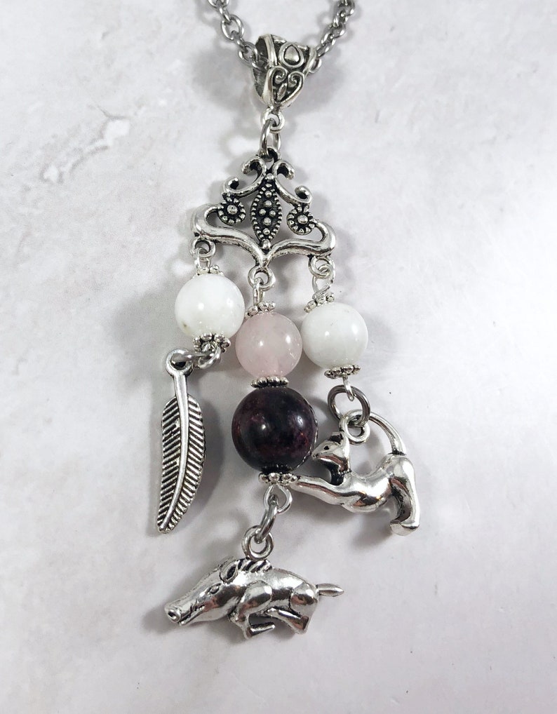 May include: A silver charm necklace with a variety of charms, including a feather, a boar, a cat, and several beads. The beads are white, pink, and dark red.