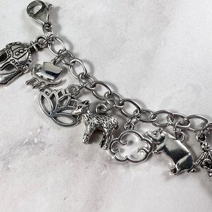 May include: A silver charm bracelet featuring a selection of charms, including a crown, a heart, a lotus flower, a deer, a cloud, a pig, and a butterfly.