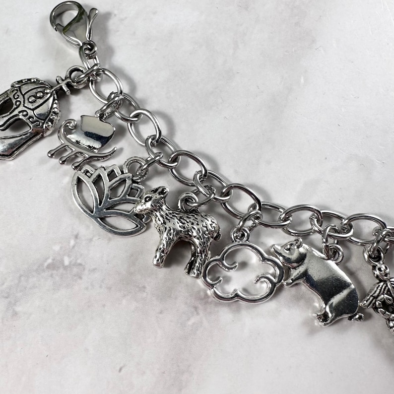 May include: A silver charm bracelet featuring a selection of charms, including a crown, a heart, a lotus flower, a deer, a cloud, a pig, and a butterfly.